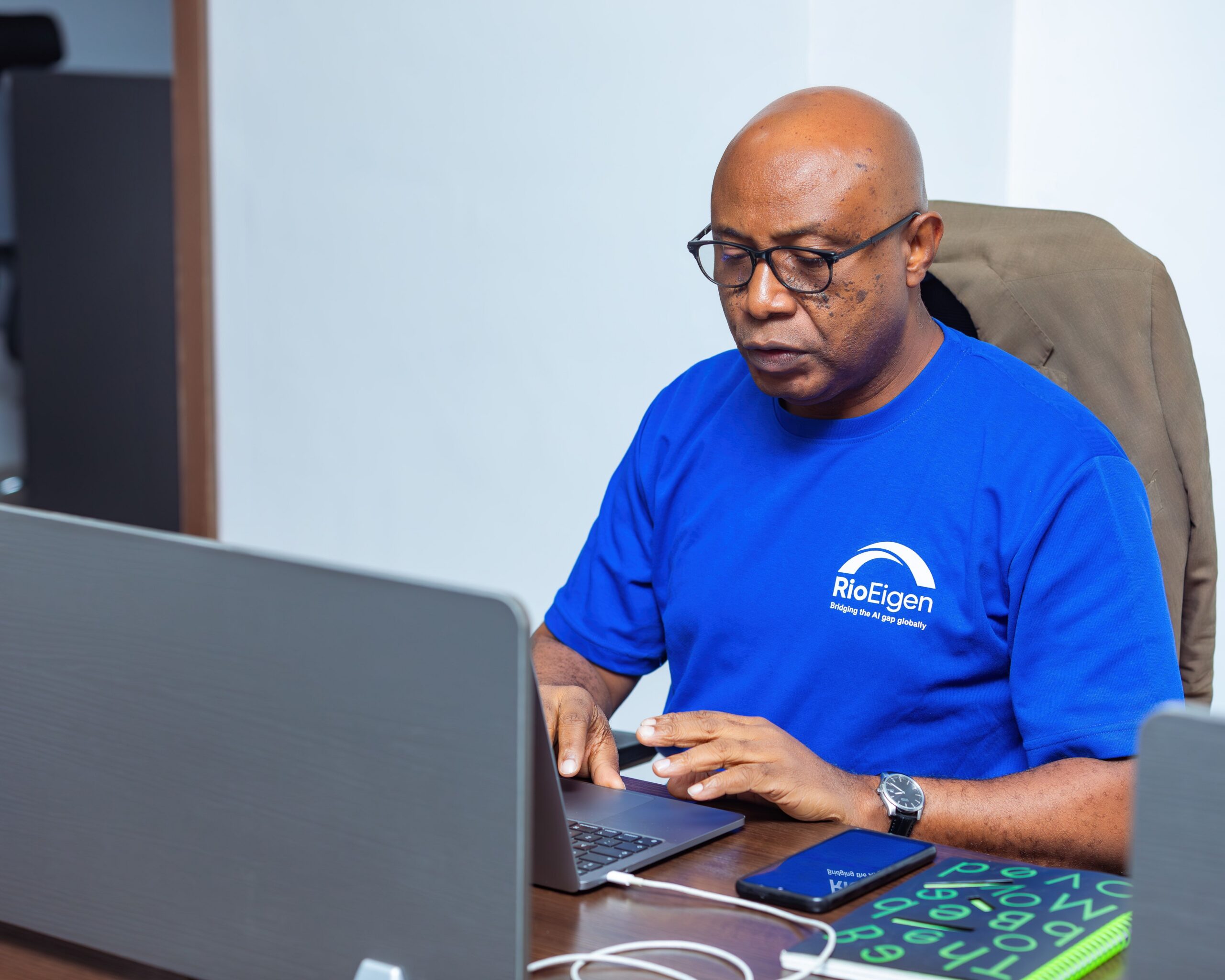 An adult man in a blue shirt working on a laptop at an office desk.